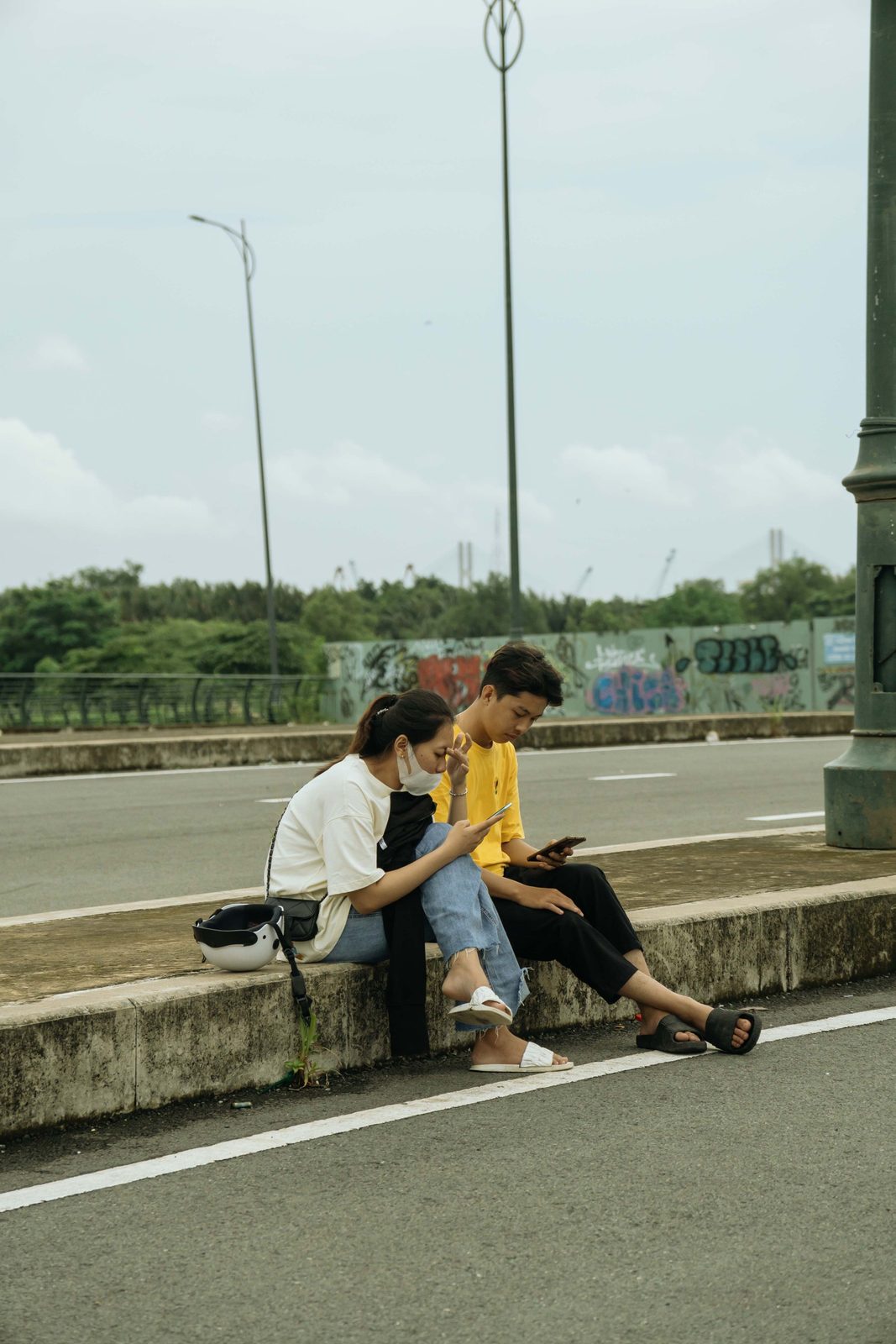 Two young people sitting at the roadside looking at a phone together